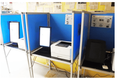 Three ImageCast X terminals in voting booths, including portrait displays and an external printer